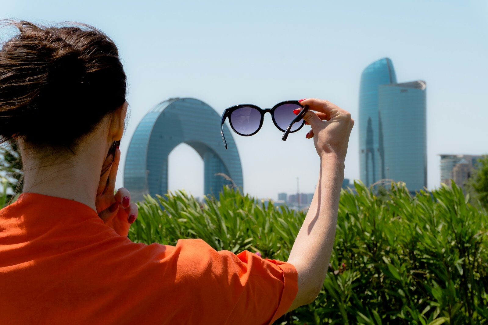 Woman holding sunglasses with city buildings behind